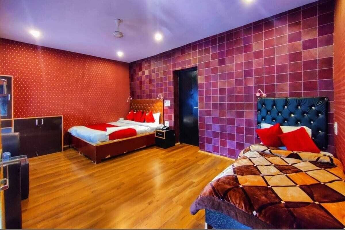 Quarto de hotel com duas camas, piso de madeira, parede com bolinhas vermelhas e parede com azulejos roxos.