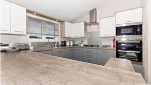 A modern kitchen with grey cabinets, a central island, a built-in oven, and a window with blinds. - Meadowbank Lodge with ceiling surround system nr beach pet friendly Shorefields (Milford on Sea)