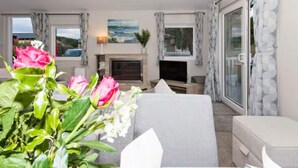A living room with a fireplace, a television, and a view of the sea through large windows. - Meadowbank Lodge with ceiling surround system nr beach pet friendly Shorefields (Milford on Sea)