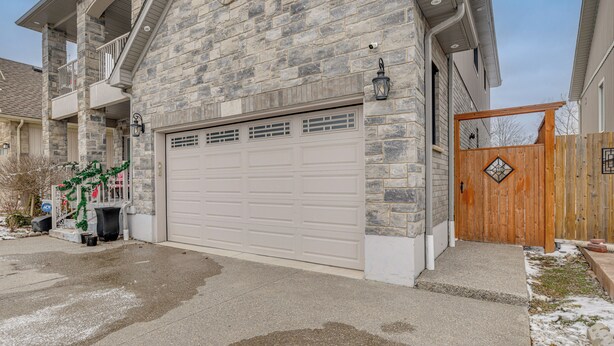 Une maison en pierre avec un garage, un portail en bois et un escalier menant à l’entrée.