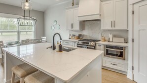 Une cuisine moderne avec des meubles blancs, un îlot central, une cuisinière à gaz et un four encastré.