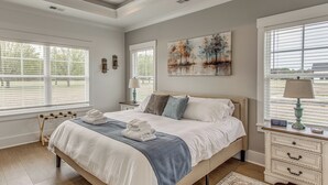 Une chambre à coucher avec un lit, des tables de chevet, une commode, un tableau et une fenêtre avec des stores.