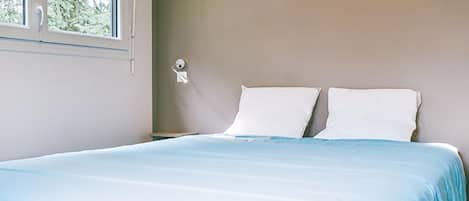 A bedroom with a bed, a window, and a wall-mounted light fixture.