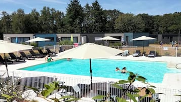 A swimming pool with lounge chairs and umbrellas, surrounded by a fenced area with trees in the background.