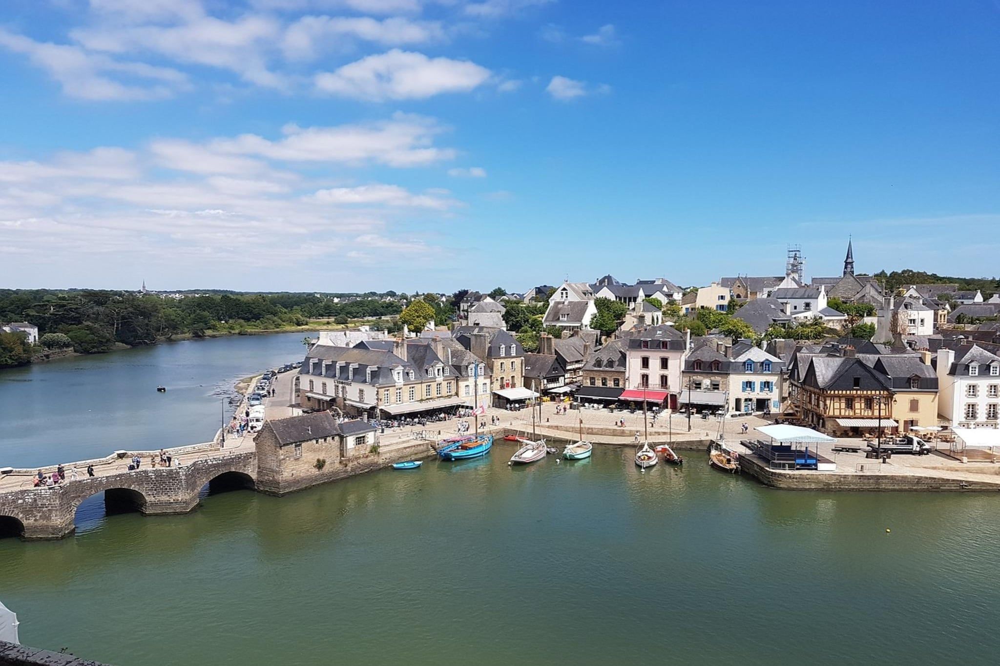 Une ville côtière avec un pont de pierre, des bâtiments donnant sur le port et des bateaux amarrés.