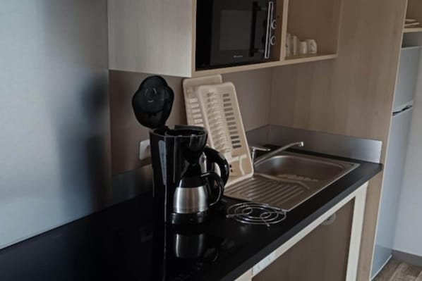 A kitchenette with a black countertop, a coffee maker, a kettle, a toaster, and a microwave.