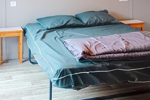 Un letto con materasso e cuscini verdi, un comodino in legno e un tavolino.