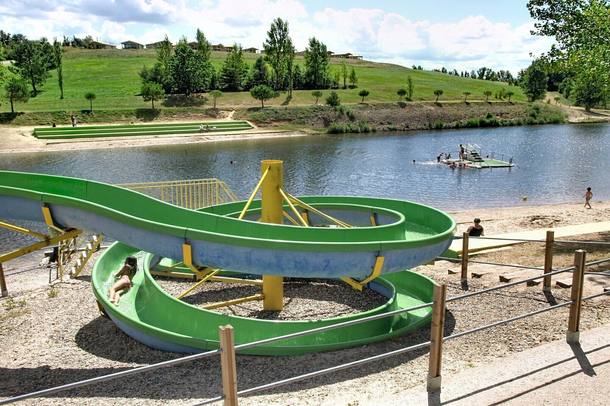 Ein Wasserpark mit einer großen, runden Wasserrutsche, einem kleinen Boot auf dem Wasser und einer grünen Rasenfläche mit Bäumen.