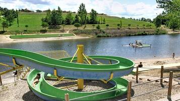 Ein Wasserpark mit einer großen, runden Wasserrutsche, einem kleinen Boot auf dem Wasser und einer grünen Rasenfläche mit Bäumen.