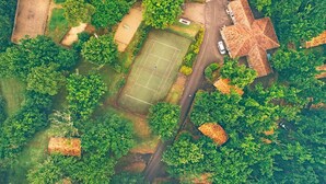 An aerial view of a property with a tennis court, a large house with a distinctive roof, and surrounding greenery. - Monclar Escape with Tennis & Shared Pool (Monclar-de-Quercy)