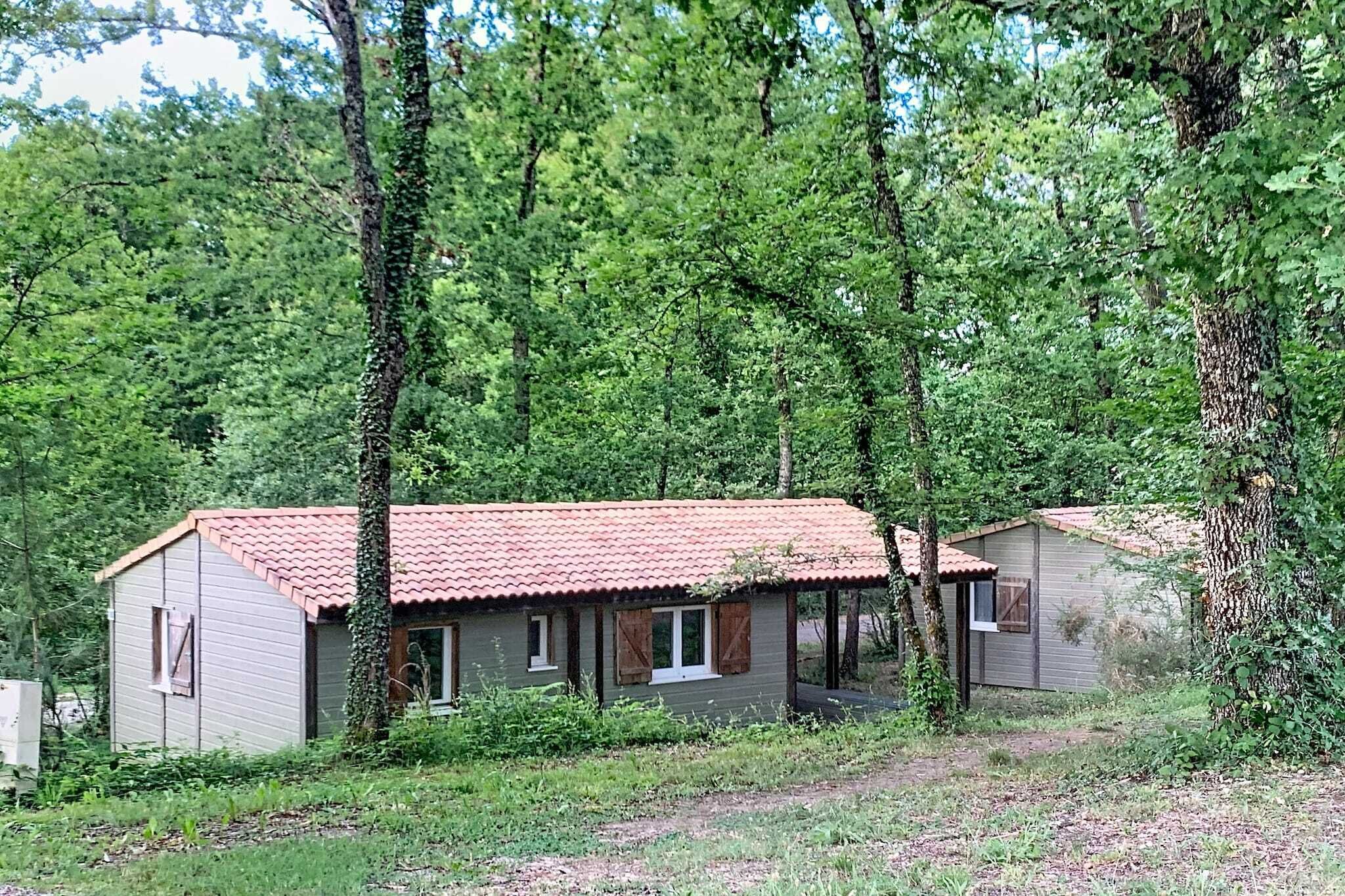 Une petite cabane à un seul étage, avec un toit recouvert de tuiles rouges, entourée d’une forêt dense.
