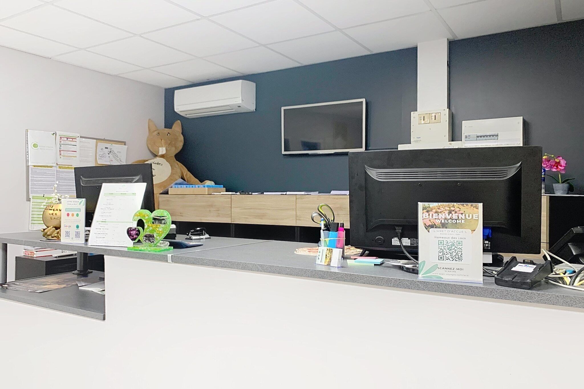 Un comptoir d’accueil orné d’une grande mascotte représentant un animal, d’un téléviseur à écran plat et d’un panneau affichant un code QR.