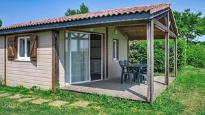 A small wooden cabin with a covered patio, a sliding glass door, and a table with chairs.