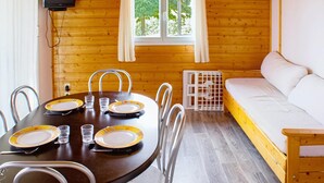 A wooden cabin interior with a dining table set for four, a sofa, and a television mounted on the wall.
