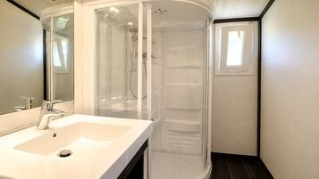A modern bathroom with a white sink, a glass-enclosed shower, and a small window.