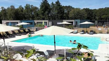 Una piscina con sillas de descanso y sombrillas, rodeada por un área cercada con árboles al fondo.