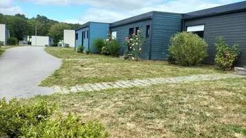 Une rangée de maisons mobiles modernes, de couleur sombre, avec une allée pavée et une zone herbeuse agrémentée de petits arbustes et de fleurs.