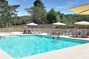 Une piscine entourée d’arbres et d’une clôture, avec des chaises longues et des parasols.