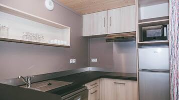 Cocina compacta con encimera negra, electrodomésticos de acero inoxidable y armarios de madera clara.