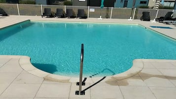 A swimming pool with a metal ladder, surrounded by a white fence and lounge chairs.