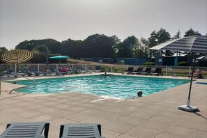 A swimming pool with lounge chairs and umbrellas, surrounded by a fence and trees.