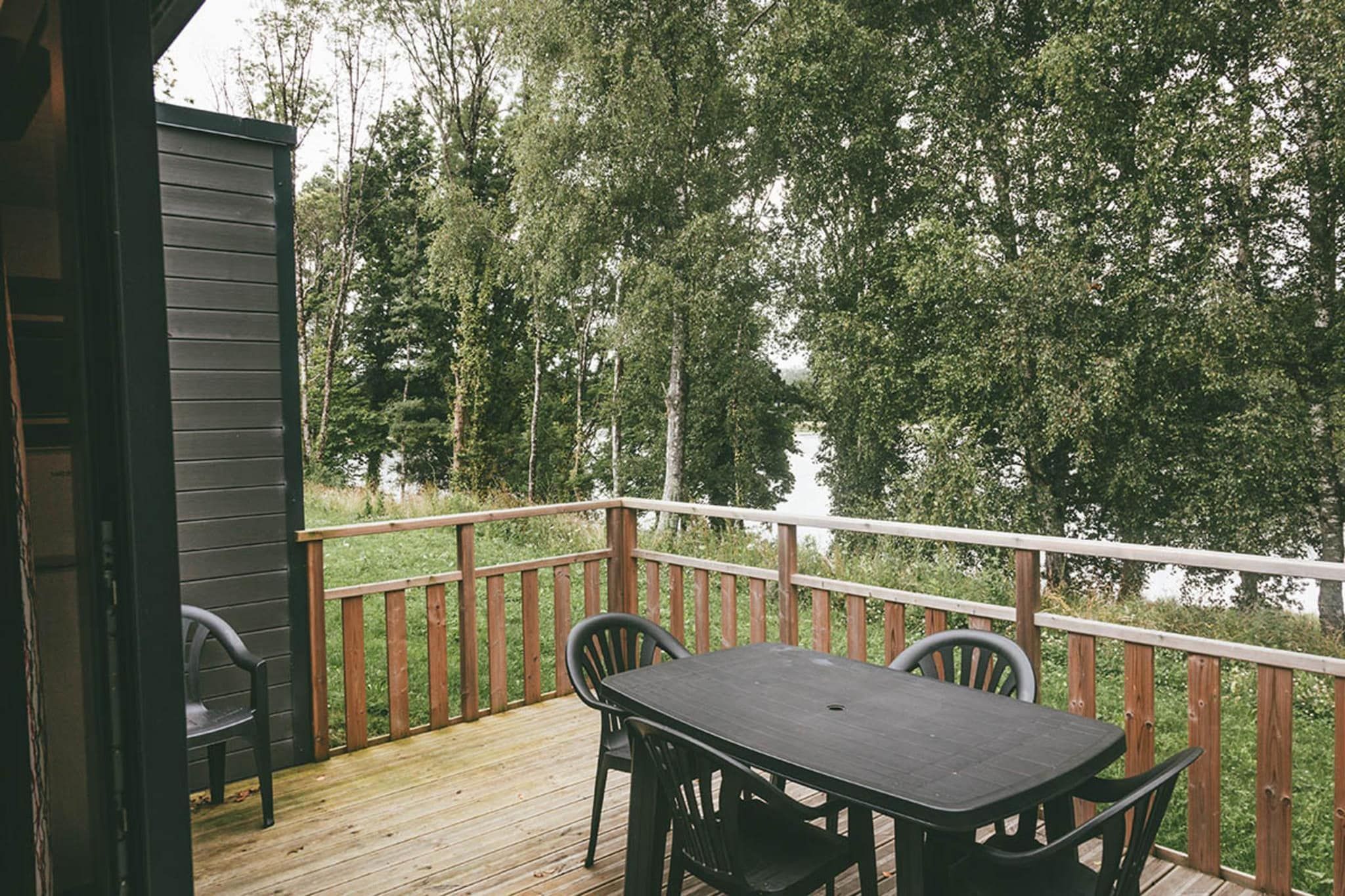 Una terraza de madera con una mesa y sillas, con vista a un área boscosa.