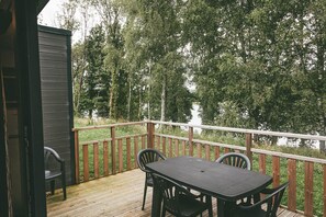 Een houten terras met een tafel en stoelen, met uitzicht op een bebost gebied.