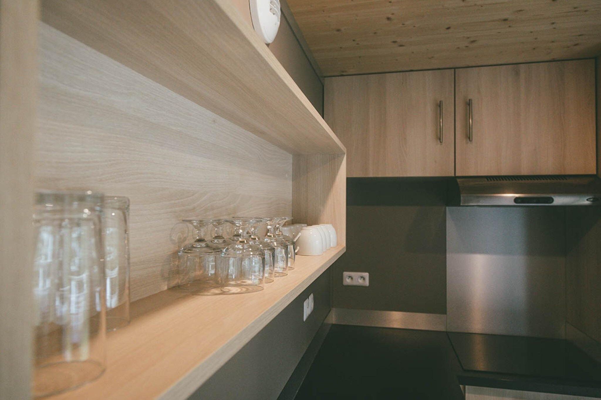 A kitchen with wooden cabinets, a stainless steel refrigerator, and a shelf with glassware.