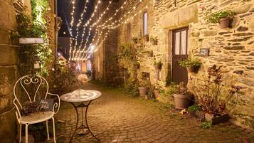 A stone building with a cobblestone courtyard, a white metal chair, a small round table, and string lights.