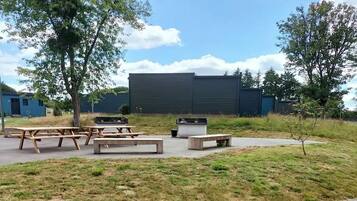 A picnic area with benches and tables, a small tree, and a building in the background.