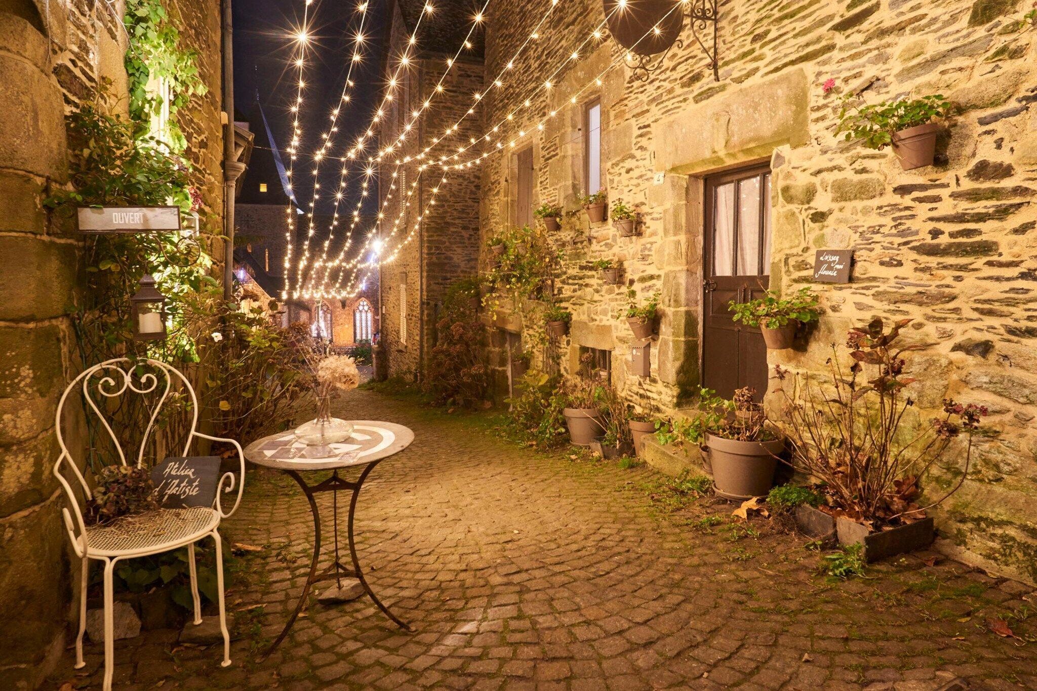 A stone building with a cobblestone courtyard, a white metal chair, a small round table, and string lights.