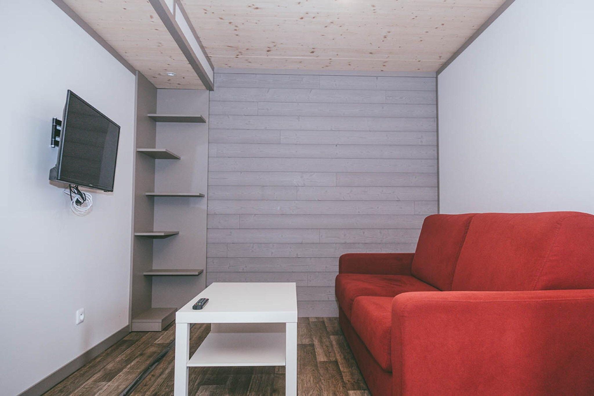 A room with a white table, a red sofa, a mounted TV, and a wooden wall.