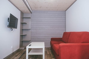 A room with a white table, a red sofa, a mounted TV, and a wooden wall.