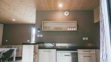 A modern kitchen with a built-in dishwasher, a wooden ceiling, and a shelf with cups.