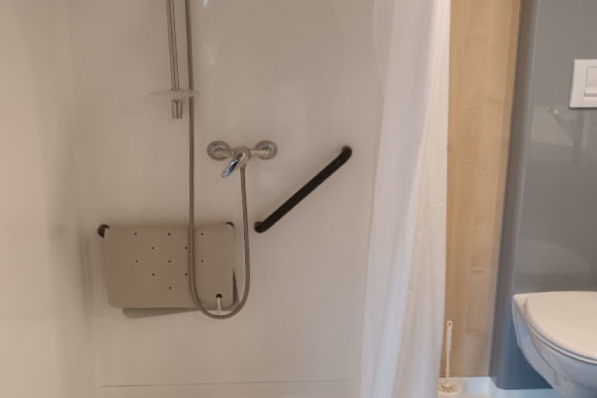 Cabina de ducha con cabezal de ducha de mano y barra de apoyo.