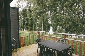 A wooden deck with a table and chairs, overlooking a forested area.