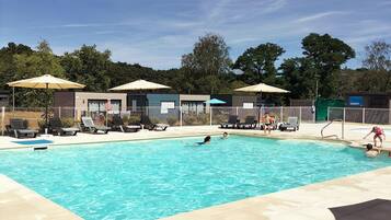 A swimming pool with lounge chairs and umbrellas, surrounded by a fence and trees.