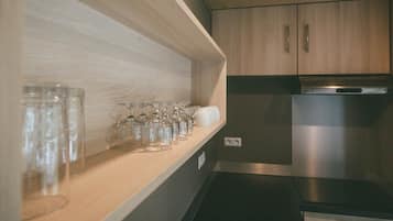 A kitchen with wooden cabinets, a stainless steel refrigerator, and a shelf with clear glasses and white cups.