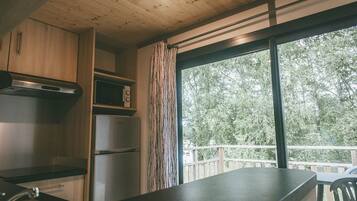 Una cocina con armarios de madera, un refrigerador de acero inoxidable, un microondas y un amplio ventanal con vista a árboles.