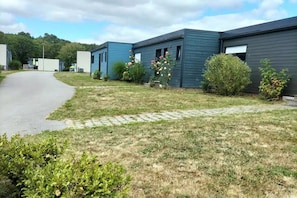 A row of modern, single-story buildings with a paved driveway leading to a grassy area with a stone pathway.