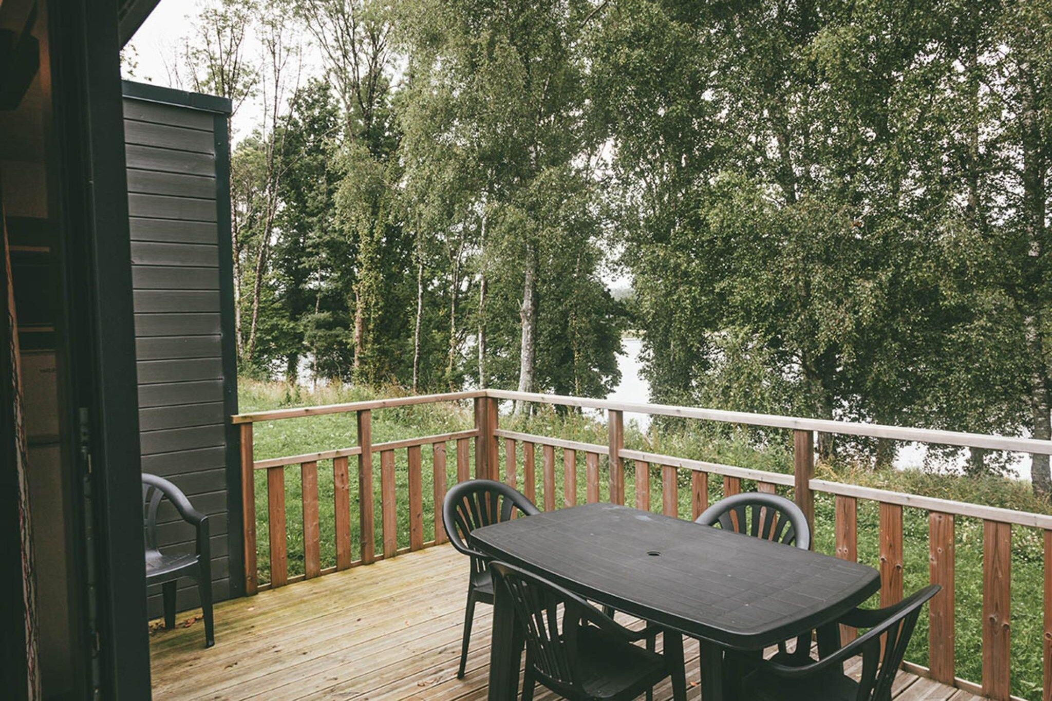 Eine Holzterrasse mit Tisch und Stühlen, mit Blick auf ein bewaldetes Gebiet.