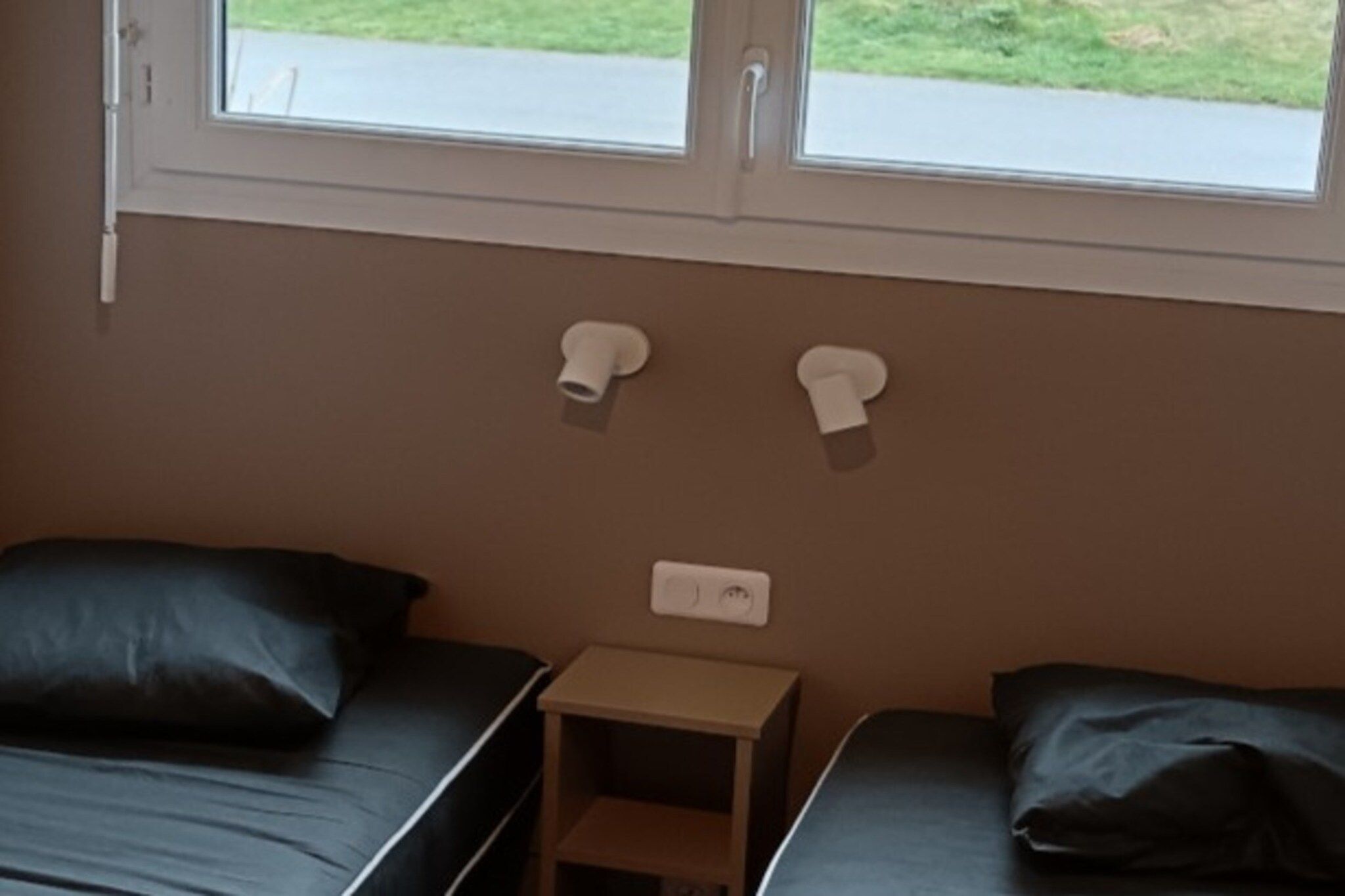 Une petite pièce avec deux lits, une table de chevet et une fenêtre.