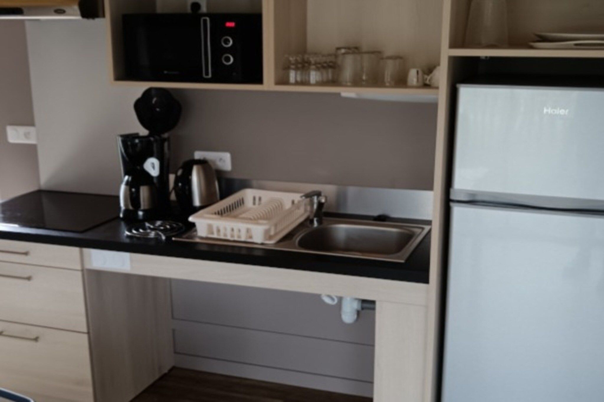 Cozinha com bancada preta, cafeteira, escorredor de louça, pia e geladeira.