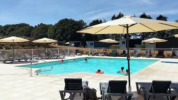 Une piscine entourée d’une clôture et d’arbres, avec des chaises longues et des parasols.