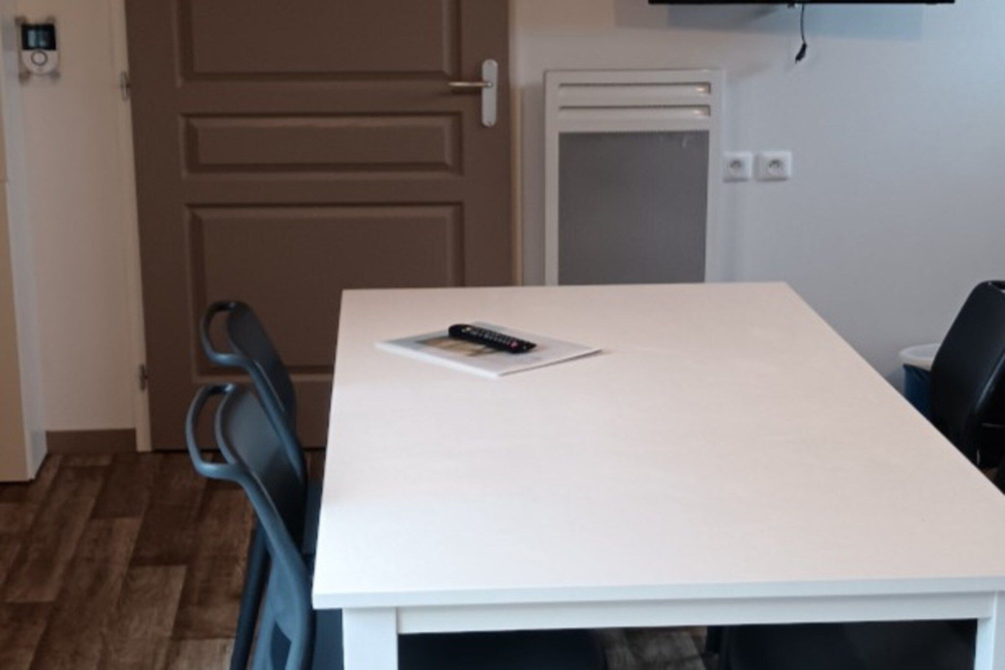 A room with a white table, a remote control on the table, and a door with a handle.