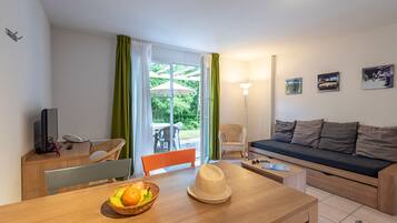 Ein möbliertes Zimmer mit einem Holztisch, einer Couch, einem Sessel, einer Lampe und einem Fenster mit Vorhängen.