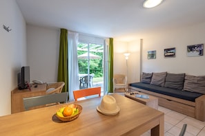 A furnished room with a wooden table, a sofa, a chair, a lamp, and a window with curtains.