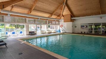 An indoor swimming pool with a wooden ceiling, clear glass walls, and a lifebuoy on the wall.