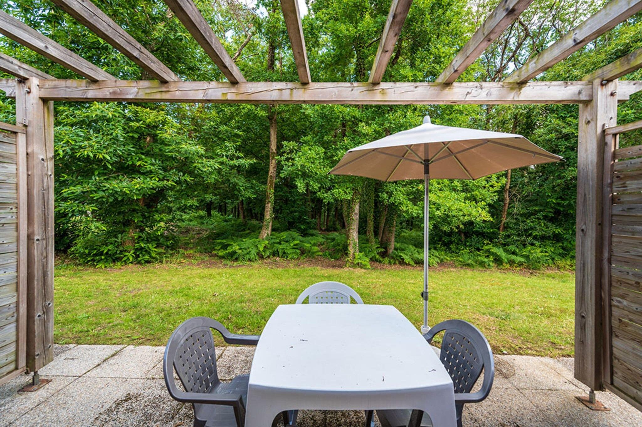 Een overdekt terras met een tafel en stoelen, omgeven door een houten pergola en uitzicht op een weelderige groene tuin.