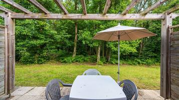 Een overdekt terras met een tafel en stoelen, omgeven door een houten pergola en uitzicht op een weelderige groene tuin.